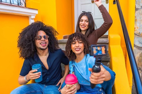 Three happy multi ethnic content creators filming a video blog with a gimbal and drinking smoothies