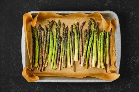 Roasted asparagus spears are neatly arranged on a baking tray lined with parchment paper