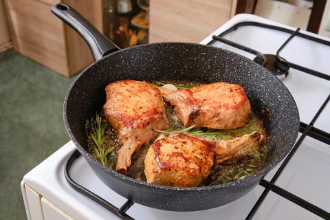 Three pork rib roasts are sizzling in a skillet, infused with fresh herbs while cooking on a