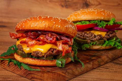 Two burgers with beef patty, fried bacon, cheddar cheese, tomatoes, homemade, no people