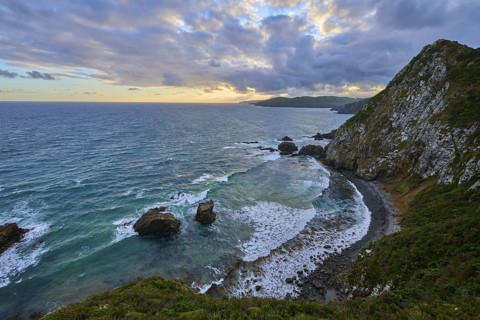 Cliffs and roaring waves in front of a colourful evening sky, summer, Nugget Point lighthouse,