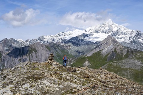Female mountaineer on hiking trail with cairn, behind glaciated and snow-covered summit of the