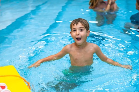 Young boy enjoying his summer vacation, playing and making funny faces in a swimming pool with a