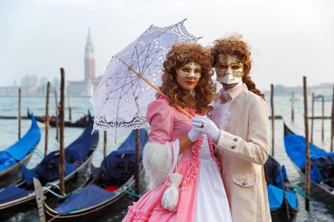 Dressed up couple, posing with masks and parasol, Venetian costumes, gondolas at St Mark's Square,