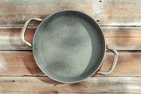 A gray frying pan with two sturdy handles on a weathered wooden tabletop. The pan is designed for