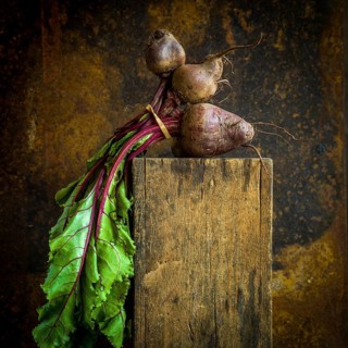 Vibrant red beets with green leaves displayed on rustic wooden surface against textured backdrop