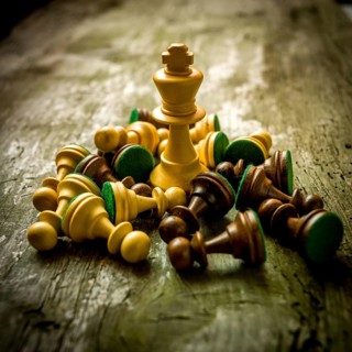 Chess pieces are strewn across a rustic wooden table, with a prominent king piece standing tall
