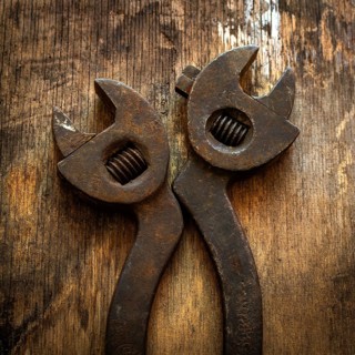 Two vintage adjustable wrenches lie side by side on a textured wooden surface, showing signs of