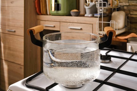 Water is boiling in a clear glass pot placed on a gas stove in a stylish kitchen. The scene