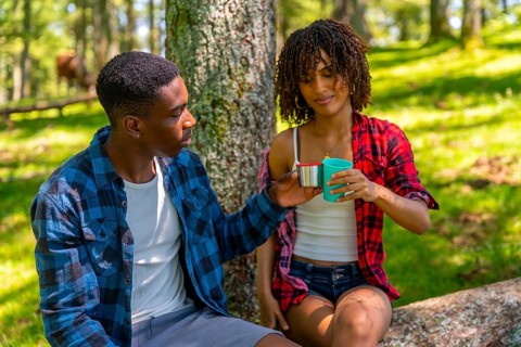 Young couple taking a refreshing break during their hike, sharing drinks from reusable cups while