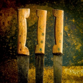 Three old, rusty kitchen knives with unevenly worn wooden handles rest against a textured backdrop.