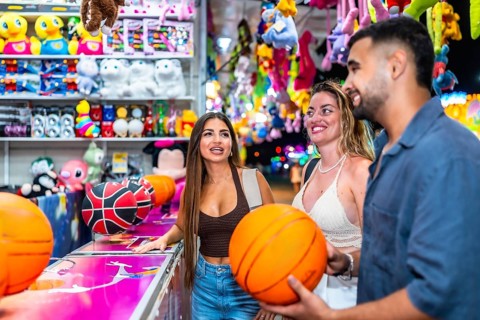 Three friends having fun playing a basketball game at an amusement park, enjoying their summer