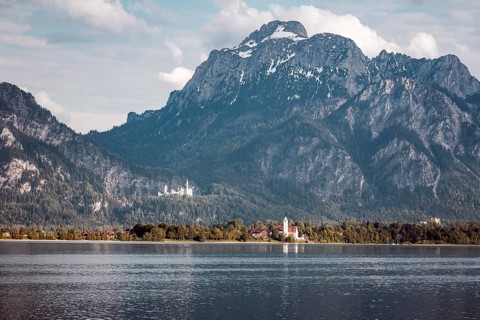A lake against an impressive mountain backdrop with Neuschwanstein Castle in the background,