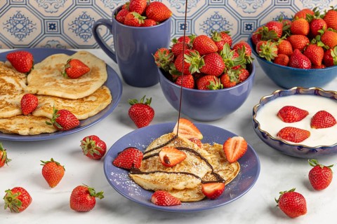 Chocolate syrup drips onto pancakes with strawberries, fresh strawberries in blue crockery in the