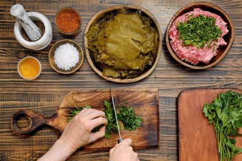 Preparing traditional dolma involves chopping herbs and meat, spreading grape leaves, and mixing