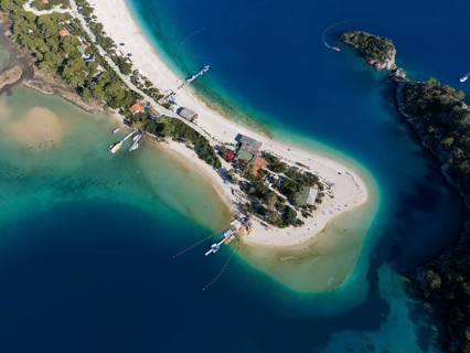 Aerial view of a small island with sandy beach and surrounding turquoise blue water and boats,