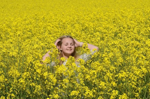 Blonde girl, 15 years old, stands smilingly in flowering rapeseed field in Ystad Municipality,