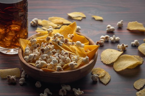 Wooden bowls with crisps and popcorn, next to a glass of cola