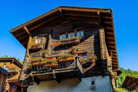 Old wooden house in log construction, decorated with flowers, historic village centre, Grimentz,