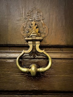 This striking door knocker blends vintage charm with intricate design, placed on a weathered wooden