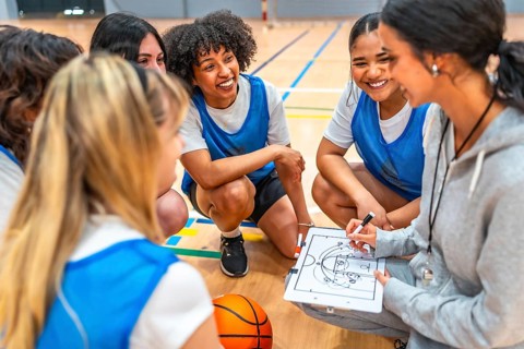 Female basketball coach drawing a play on a clipboard while explaining game strategy to her team