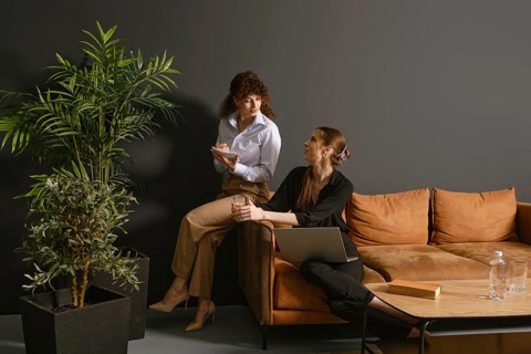 Two women engage in a lively discussion in a contemporary office. One holds a notepad while sitting