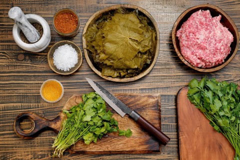 Preparing dolma by assembling marinated grape leaves, ground meat, and herbs on a wooden countertop
