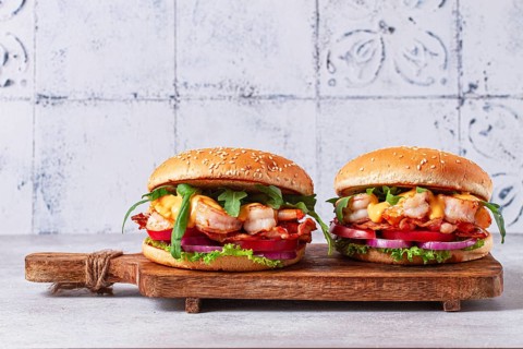 Two shrimp burgers and buns with sesame seeds, bacon, lettuce, tomatoes and onions, On a wooden