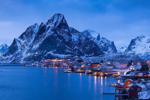 Fishermen's Village in front of snowy mountain range at the coastline in winter, Lofoten, Norway