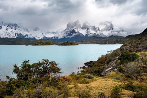 Cloudy mountain range Cuernos del Paine, shore of the blue lake Lago Pehoe in the evening light,