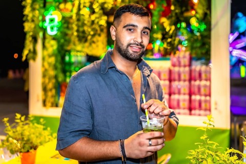 Stylish man savoring a vibrant mojito cocktail at a bustling night market, surrounded by colorful