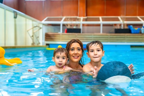 Happy mother enjoying time in the swimming pool with her sons, playing joyfully with colorful