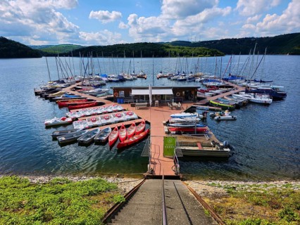 A colourful little marina with boats, sailing boats and pedal boats docked at a jetty on a lake,