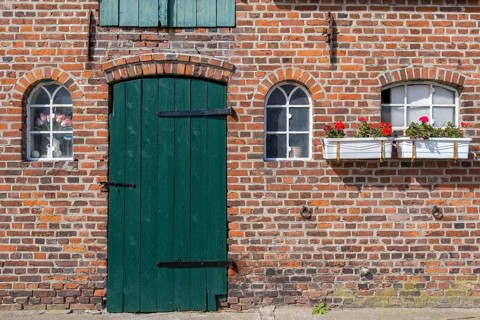 Nostalgic brick wall with green door and white windows, decorated with flower pots, Föhr,