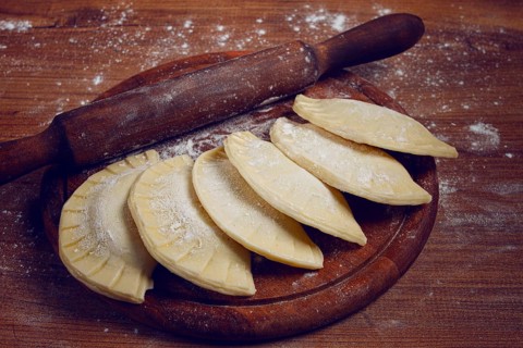 Raw chebureks, mini, on a cutting board, wooden table, close-up, no people