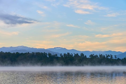 A peaceful lake with a misty surface and mountains in the morning light, Lake Mahinapua, Ruatapu,