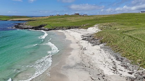 An idyllic coastal landscape with a sandy beach and green meadow under a blue sky, Meal Beach,
