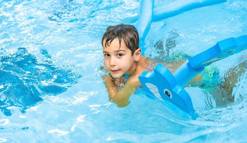 Happy boy enjoying playtime with an inflatable toy whale in a sparkling swimming pool, soaking up