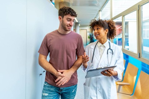 Doctor holding clipboard and explaining diagnosis to patient while walking in hospital corridor