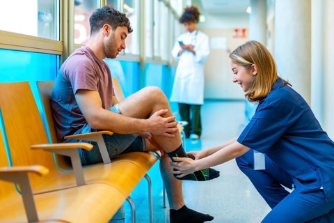 Young man sitting in a hospital waiting area receives assistance from a nurse who is putting a