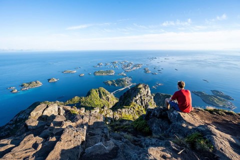 View of numerous small rocky islands with houses, mountaineers on the summit of Festvågtind, view