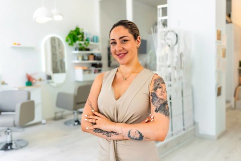 Portrait of a smiling hairdresser standing with arms crossed in her modern beauty salon, proud