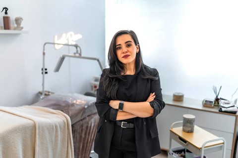 Confident female beautician posing with crossed arms in her modern beauty salon, featuring a laser