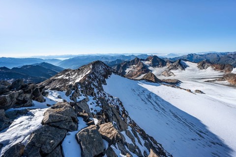 Narrow rocky ridge at the Wilder Freiger summit, picturesque high mountain landscape with snow,