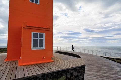 Orange lighthouse Skálasnagaviti or Svörtuloft with wooden plank path, walker, Skalasnagi,