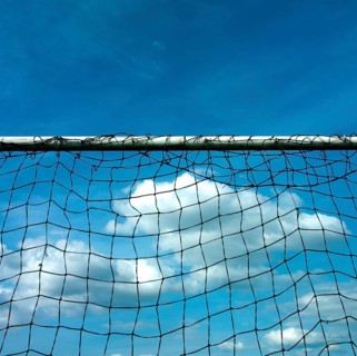 A football goal net stands prominently against a backdrop of a cloudy sky. The bright blue sky adds