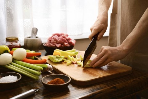 Hands skillfully cut bell pepper on a wooden board in a bright kitchen. Fresh meat and various