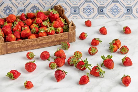 Strawberries scattered on a marble slab, next to a box full of strawberries