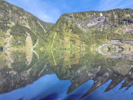 Mountains with reflections in the water against a blue sky in Doubtful Sound, South Island, New