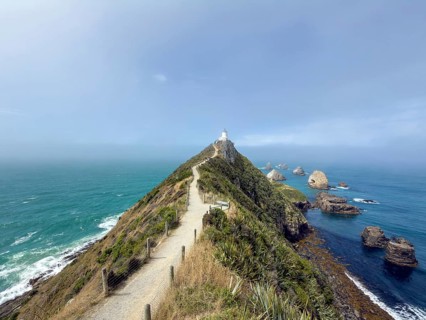 Nugget Point Lighthouse with Nugget Rocks in front of a blue sky, South Island, New Zealand,